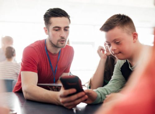 Point of view angle of teacher assisting down syndrome boy with using the smart phone.